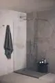 Dusche mit Glasabtrennung und Regenbrause in einem modern gestalteten Raum. Die Ausstattung zeigt eine elegante Handbrause und eine Ablage mit Pflegeprodukten von Ideal Standard.